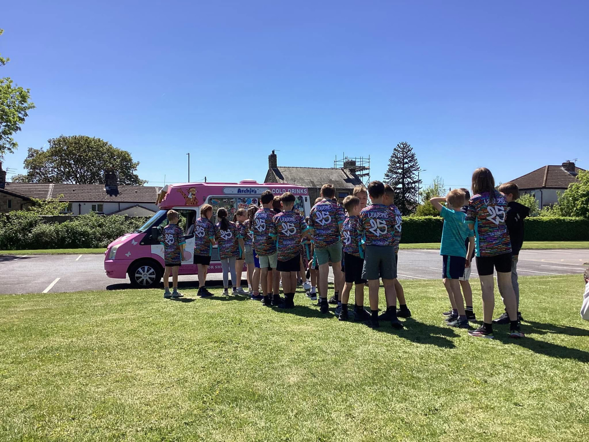Children in black and teal 22 Unite shirts queuing at an ice cream van