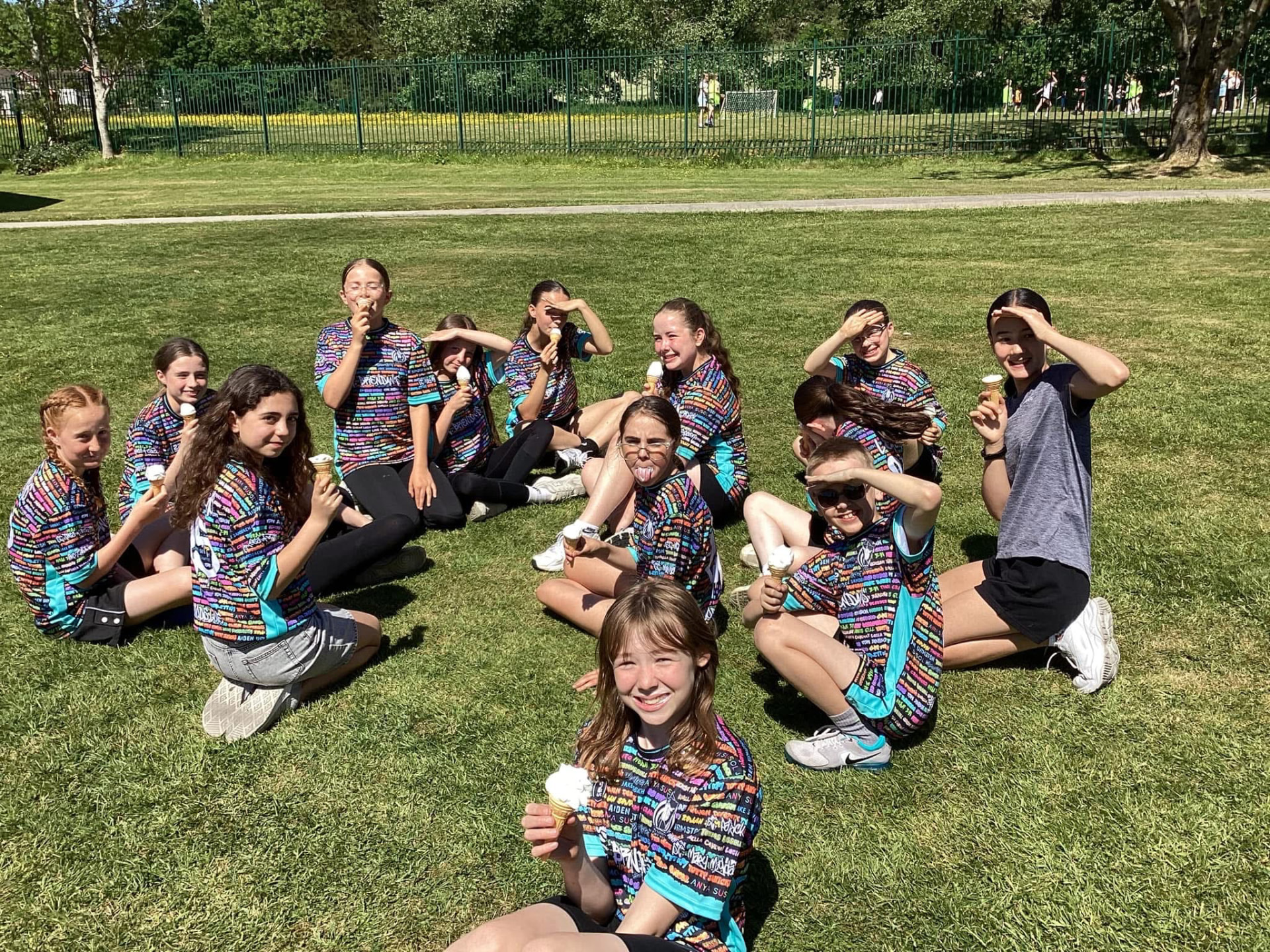 Children in black and teal 22 Unite shirts sitting in a circle on grass